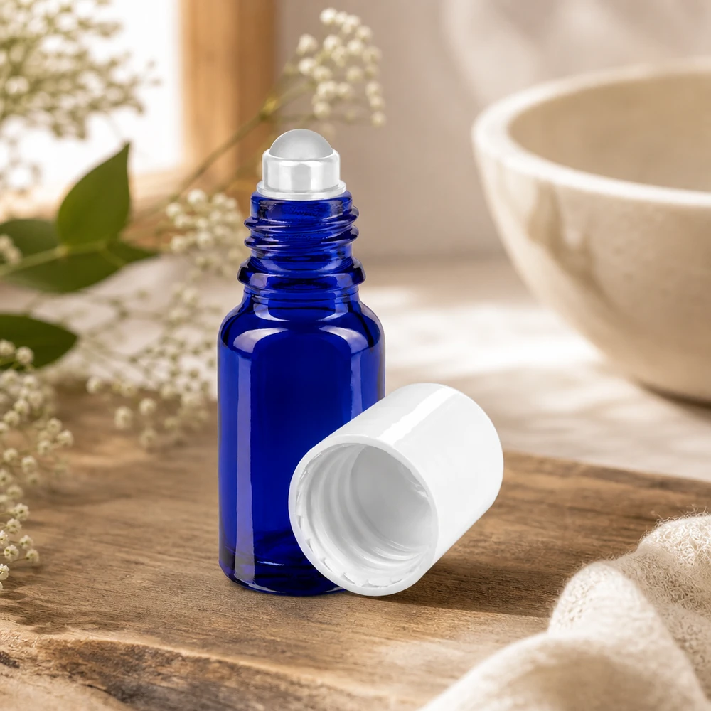 Blaue 10ml Apothekerglasflasche mit Rollapplikator neben Keramikschale und Naturblüten