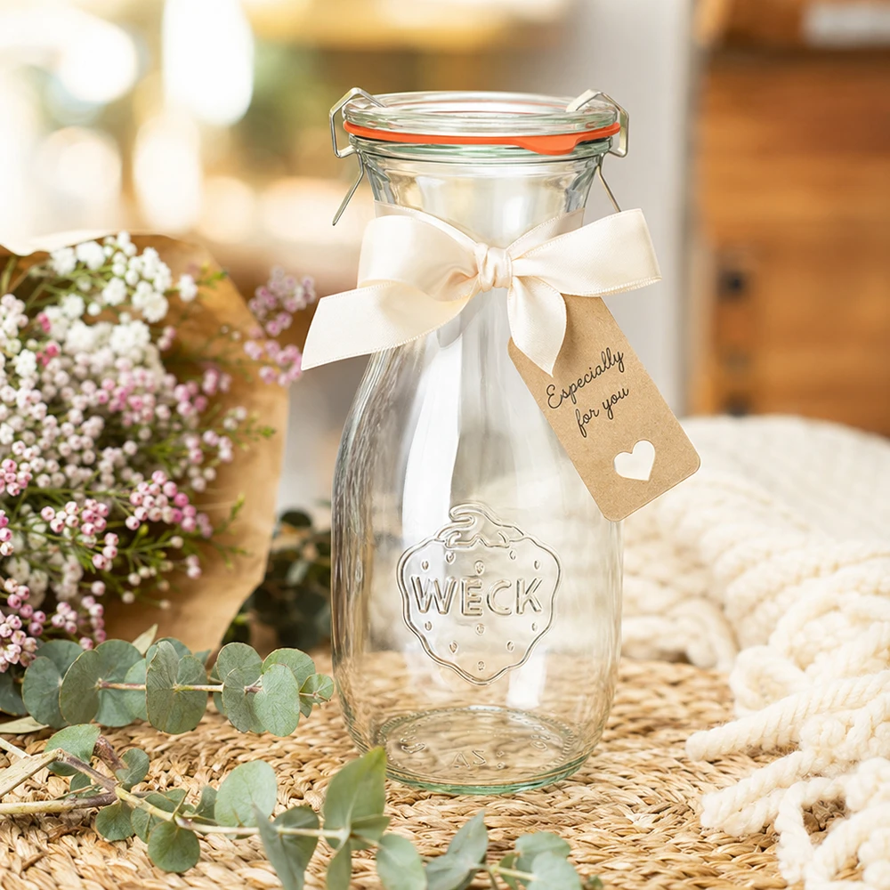 WECK 530ml Saftflasche RR60 dekorativ mit weißer Schleife und Geschenkanhänger zwischen Blumen arrangiert