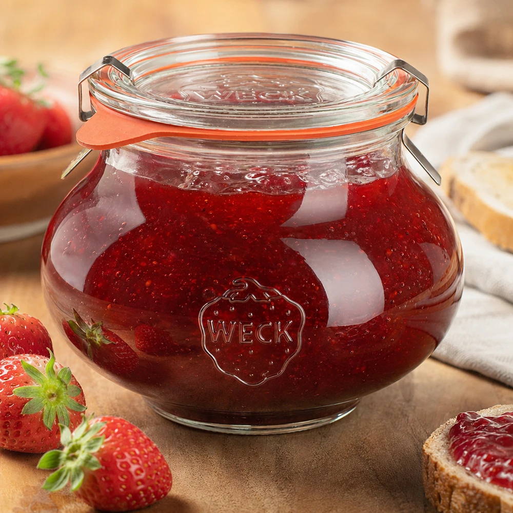 WECK Schmuckglas 560ml mit selbstgemachter Erdbeermarmelade gefüllt, Bügelverschluss geschlossen, umgeben von frischen E