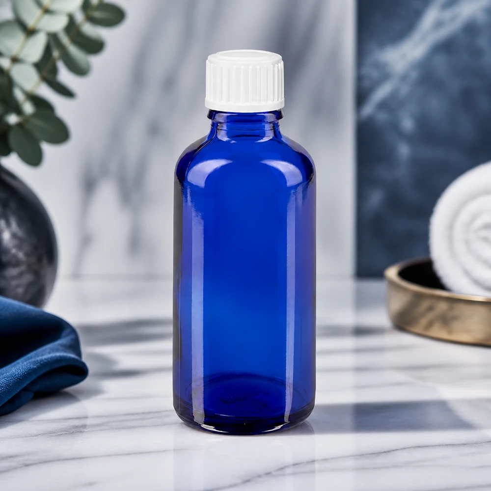Apothekenflasche blau 50ml Tropfverschluss weiß 0.8mm Standard Blaue 50ml Rundflasche ApoGlas mit gerilltem weißen Verschluss vor elegantem Marmor-Hintergrund