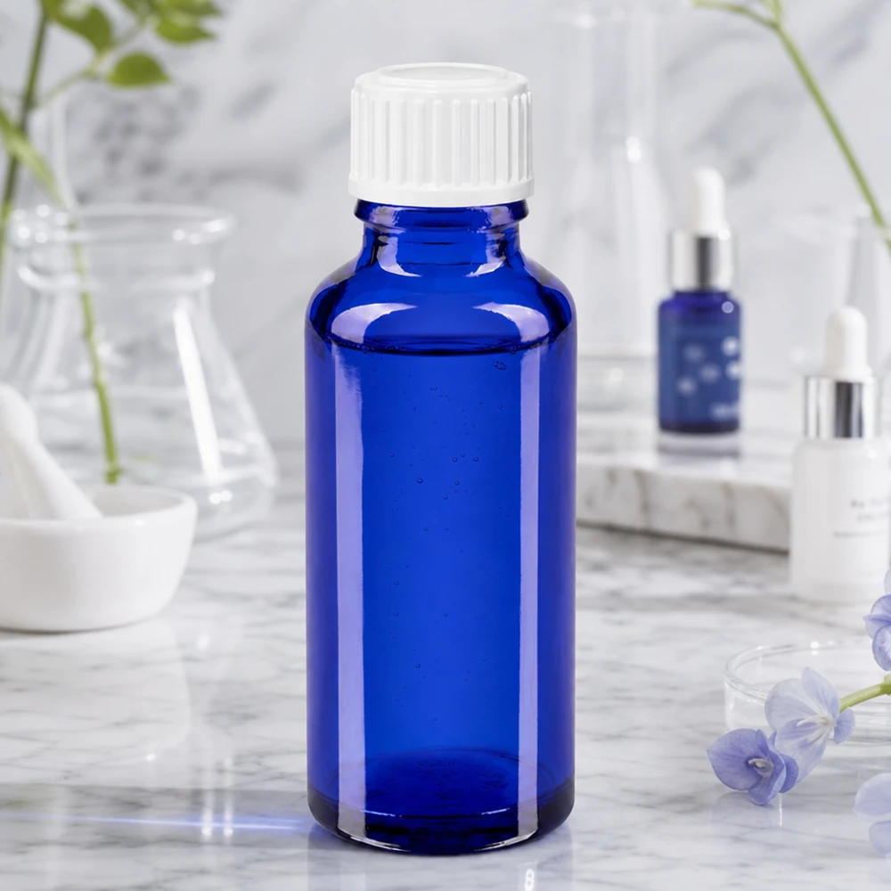 Blaues Pharmaglas 30ml mit weißem Verschluss neben Kosmetikprodukten und Glasgefäßen