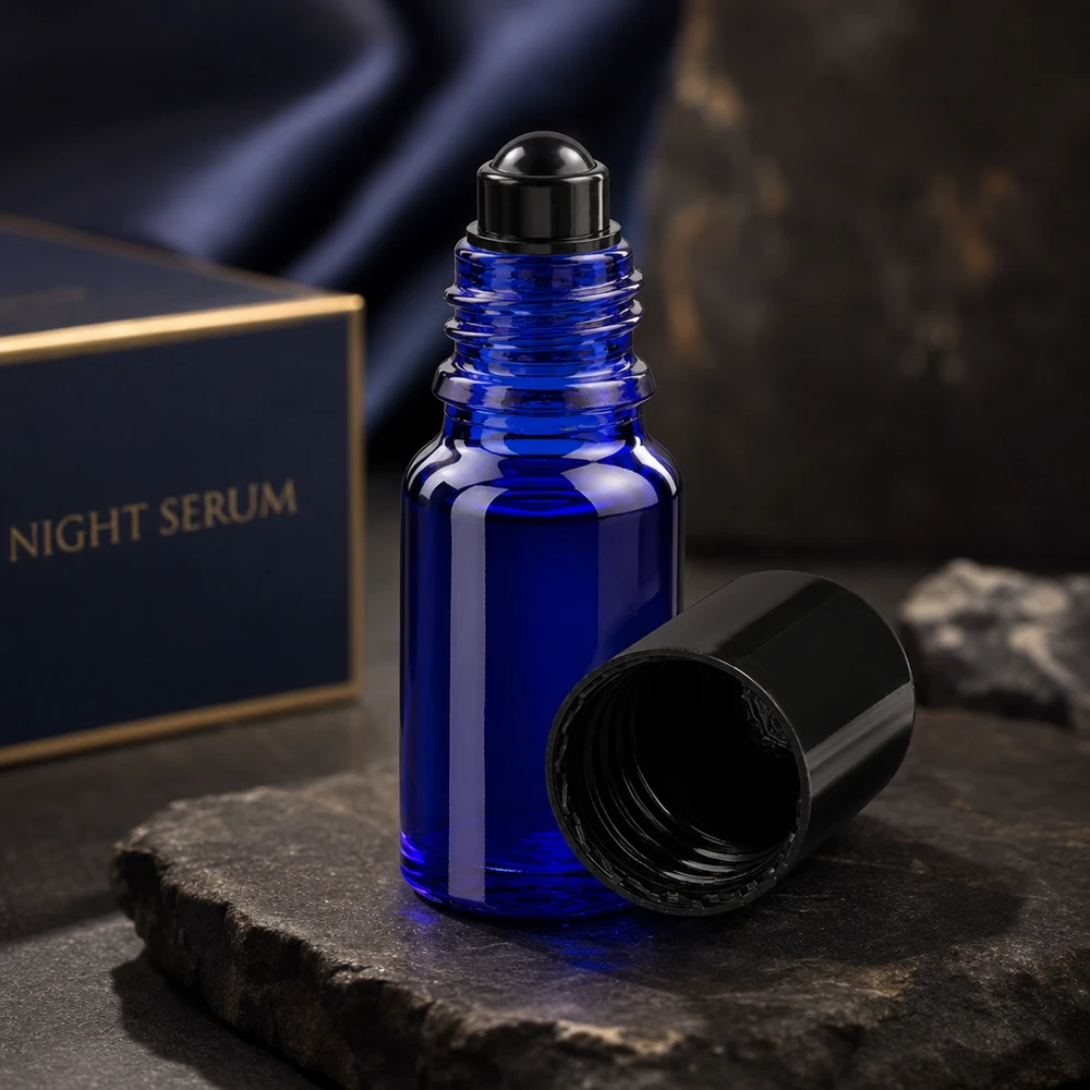 Geöffnete kobaltblaue 10ml Glasroller Flasche mit schwarzem Schraubverschluss auf dunklem Steinhintergrund