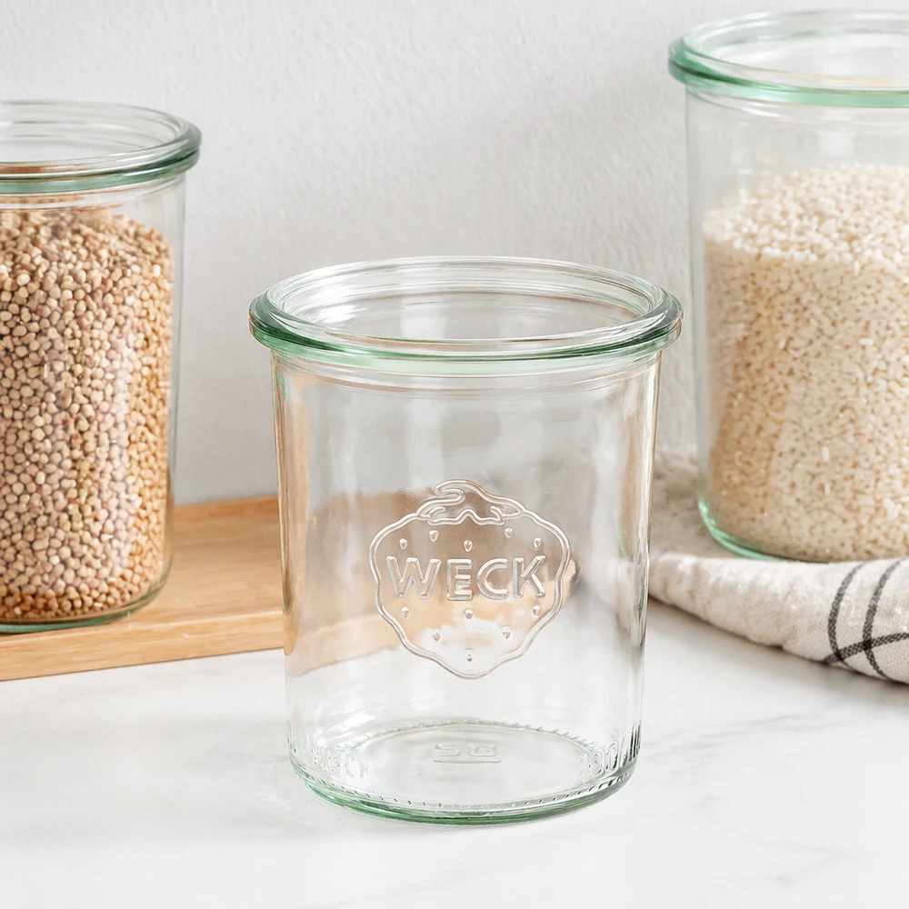 160ml Sturzglas WECK RR60 WECK Sturzglas 160ml RR60 mit grünem Rand und Logo, leeres Einmachglas neben gefüllten Vorratsgläsern auf Holzbrett